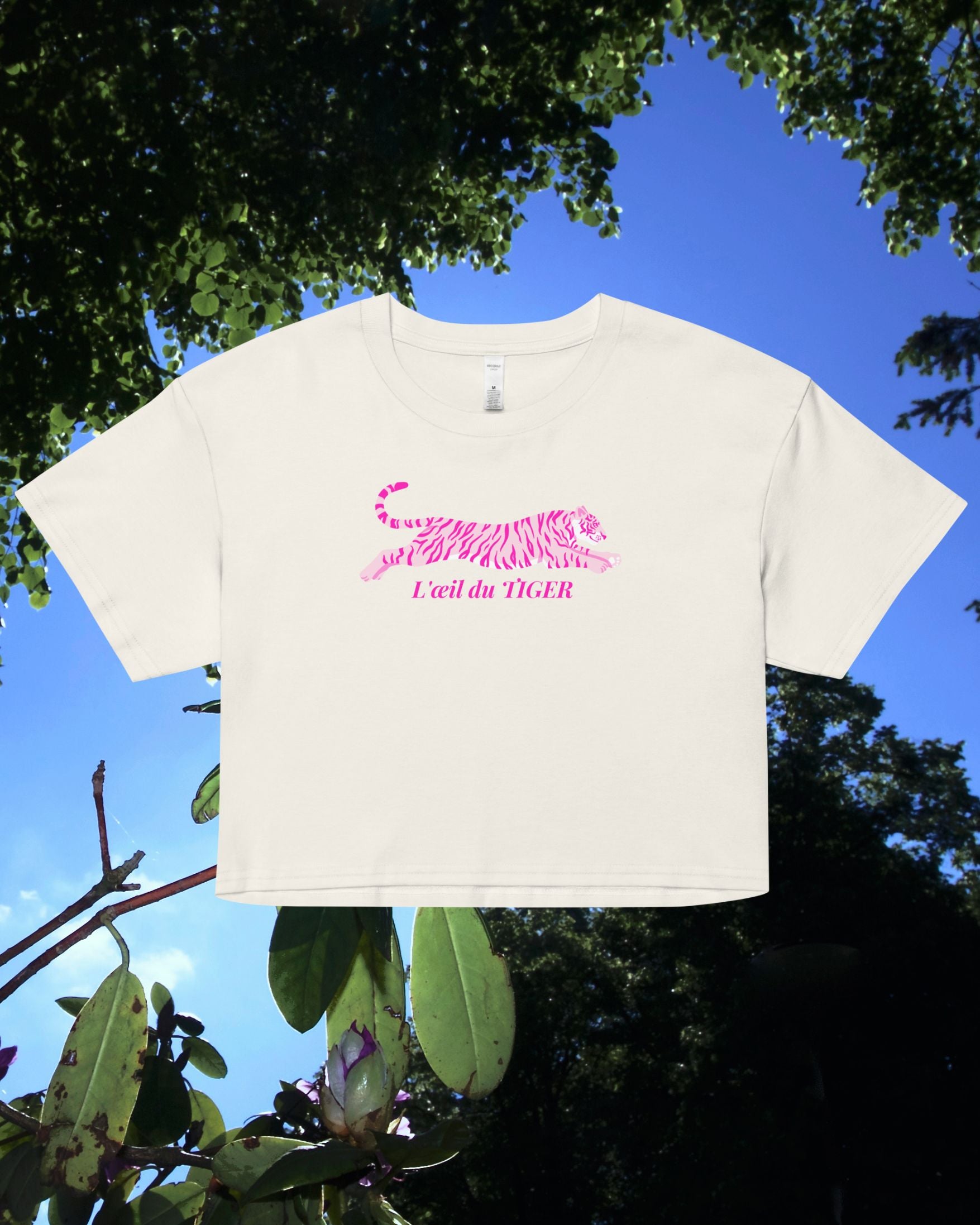 White crop top with pink text against a blue sky and green foliage background