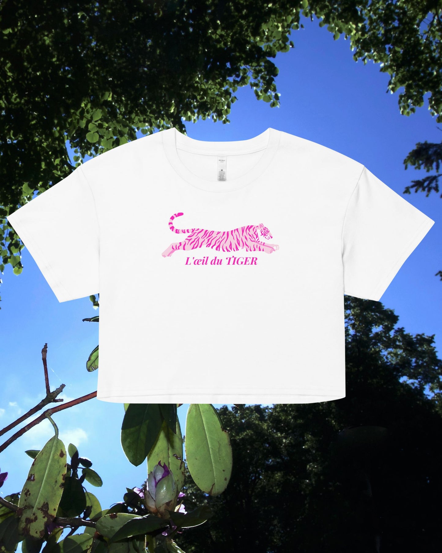 White t-shirt with pink tiger design and text against a blue sky and green foliage background