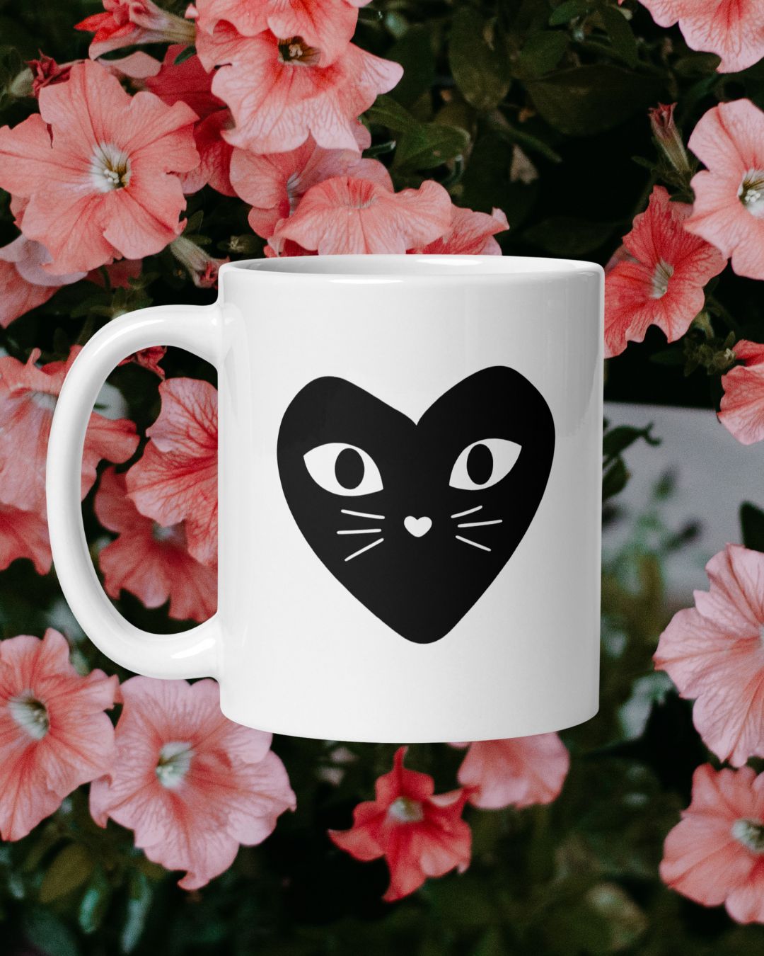 White mug with black heart-shaped cat face design against a floral background