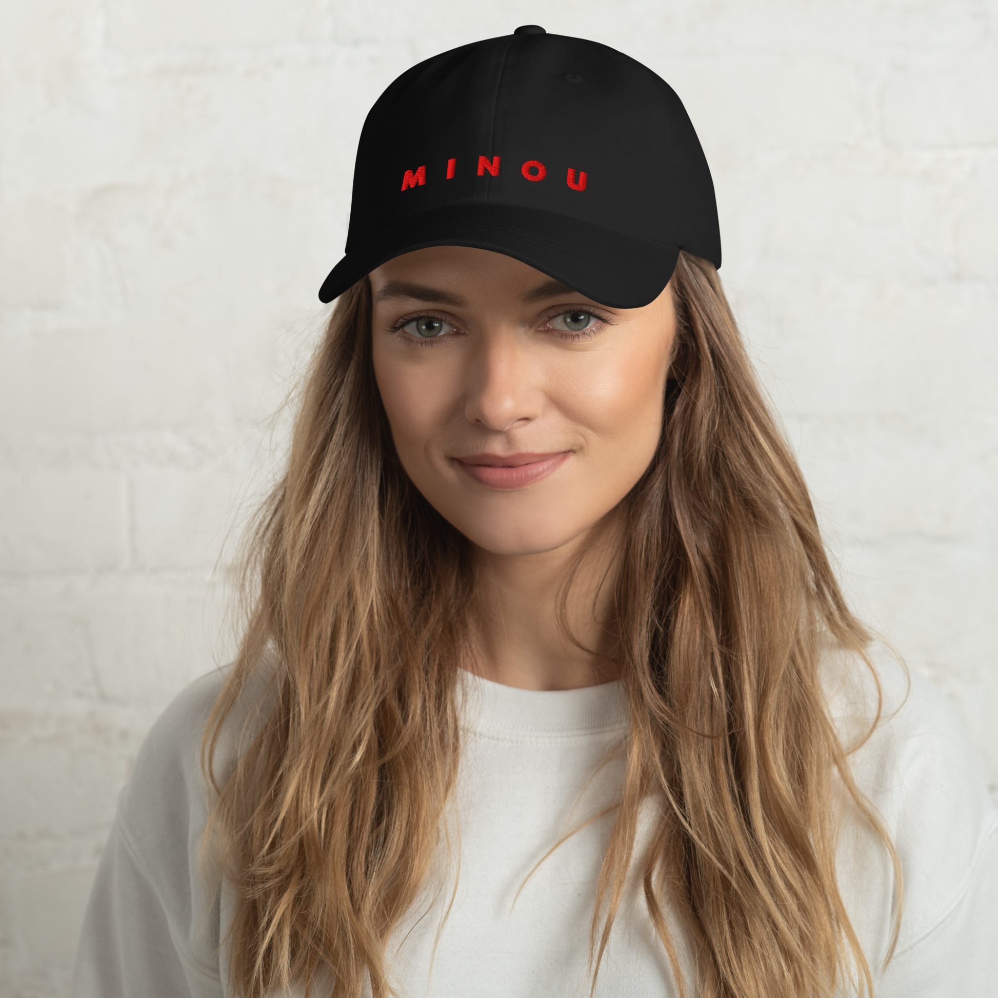 Person wearing a black cap with 'MINOU' in red on a white background