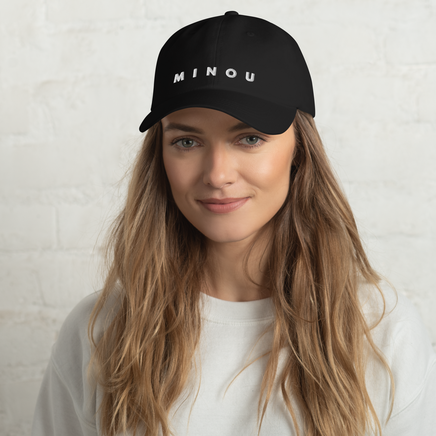 Woman wearing a black cap with 'MINOU' text on a white background