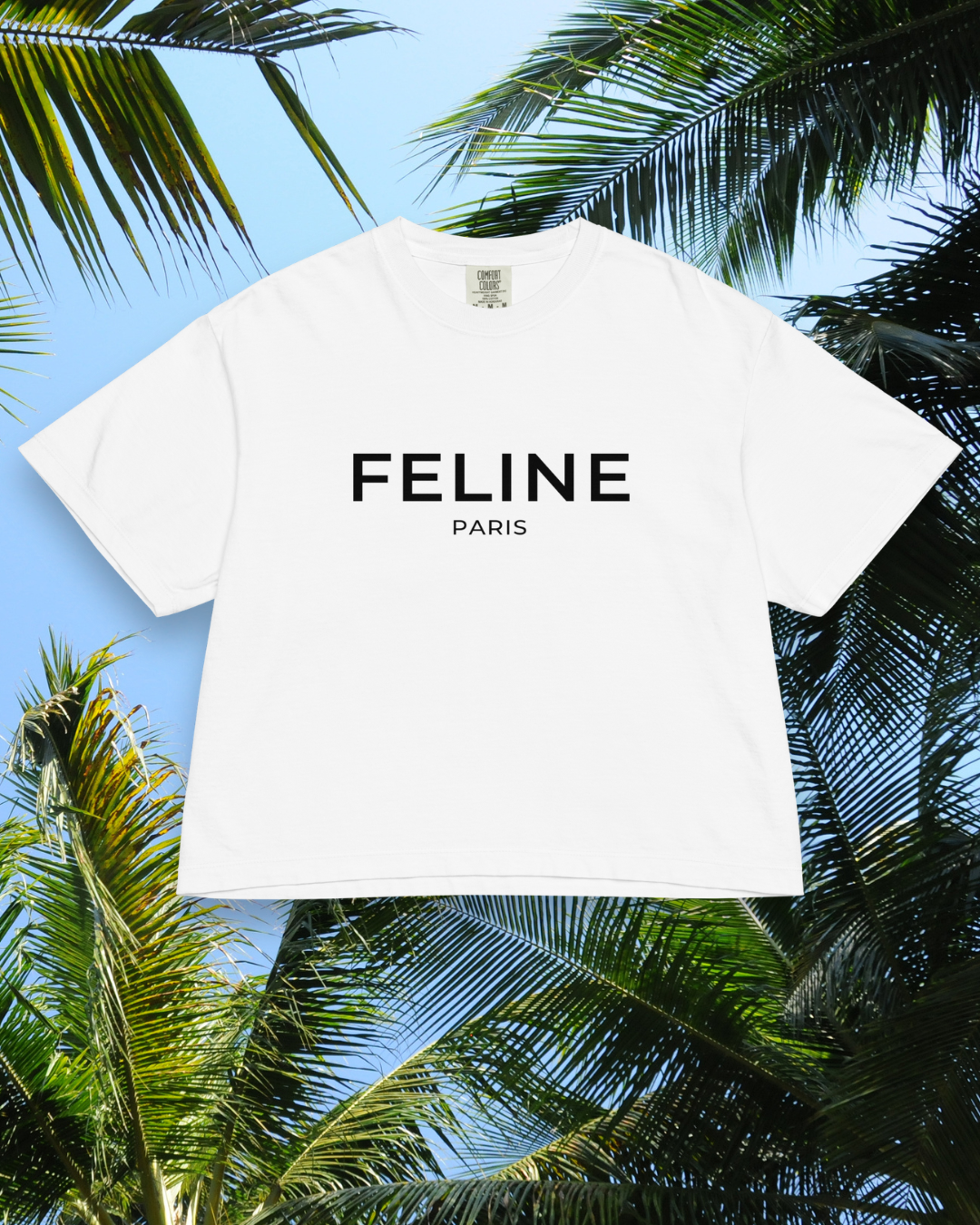White t-shirt with 'FELINE PARIS' text against a tropical background with palm leaves.
